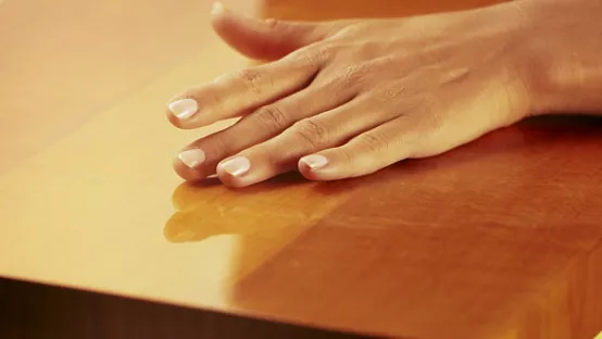 A hand feeling a smooth wood table with a yellow background. / Fotolia Image # 25043188