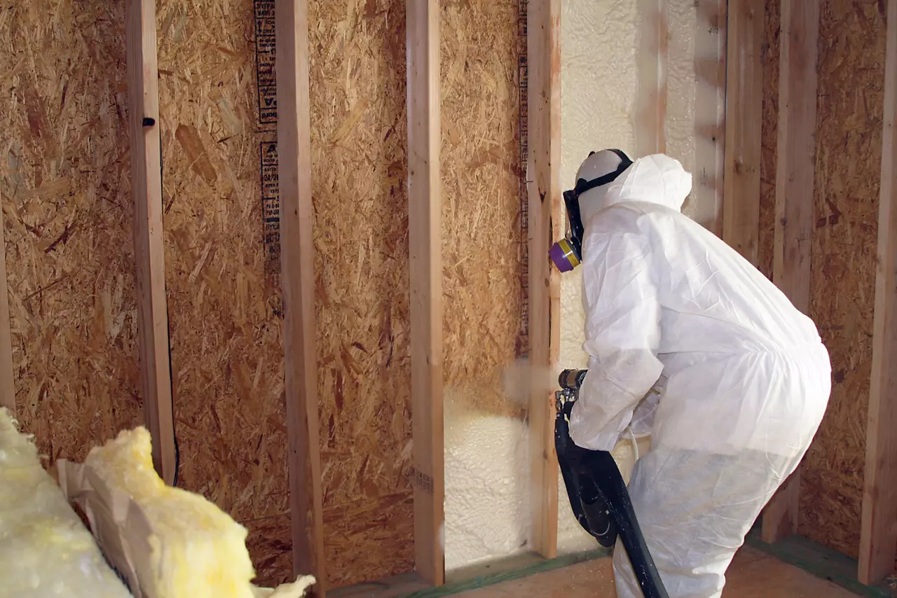 Man in protective white suit and respirator applying insulation.