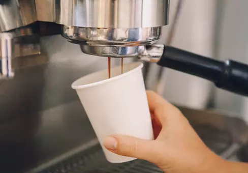Closeup of young Caucasian barista hands holding paper cup making coffee 