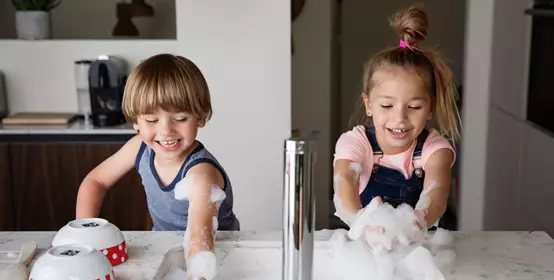Kids playing with suds while washing dishes in a modern sink