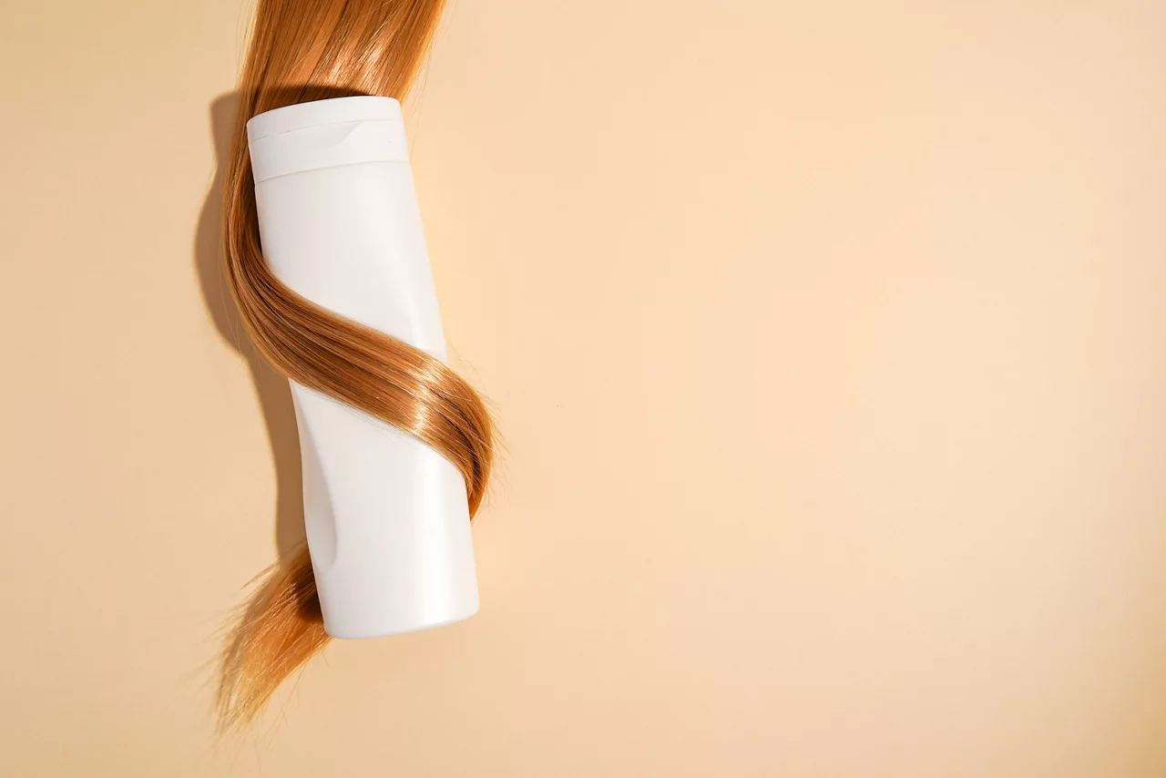 Blond hair curled around shampoo bottle close-up on light background, copy space