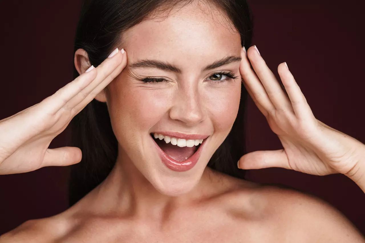 Image of smiling half-naked woman touching her temples and winking isolated over dark red background